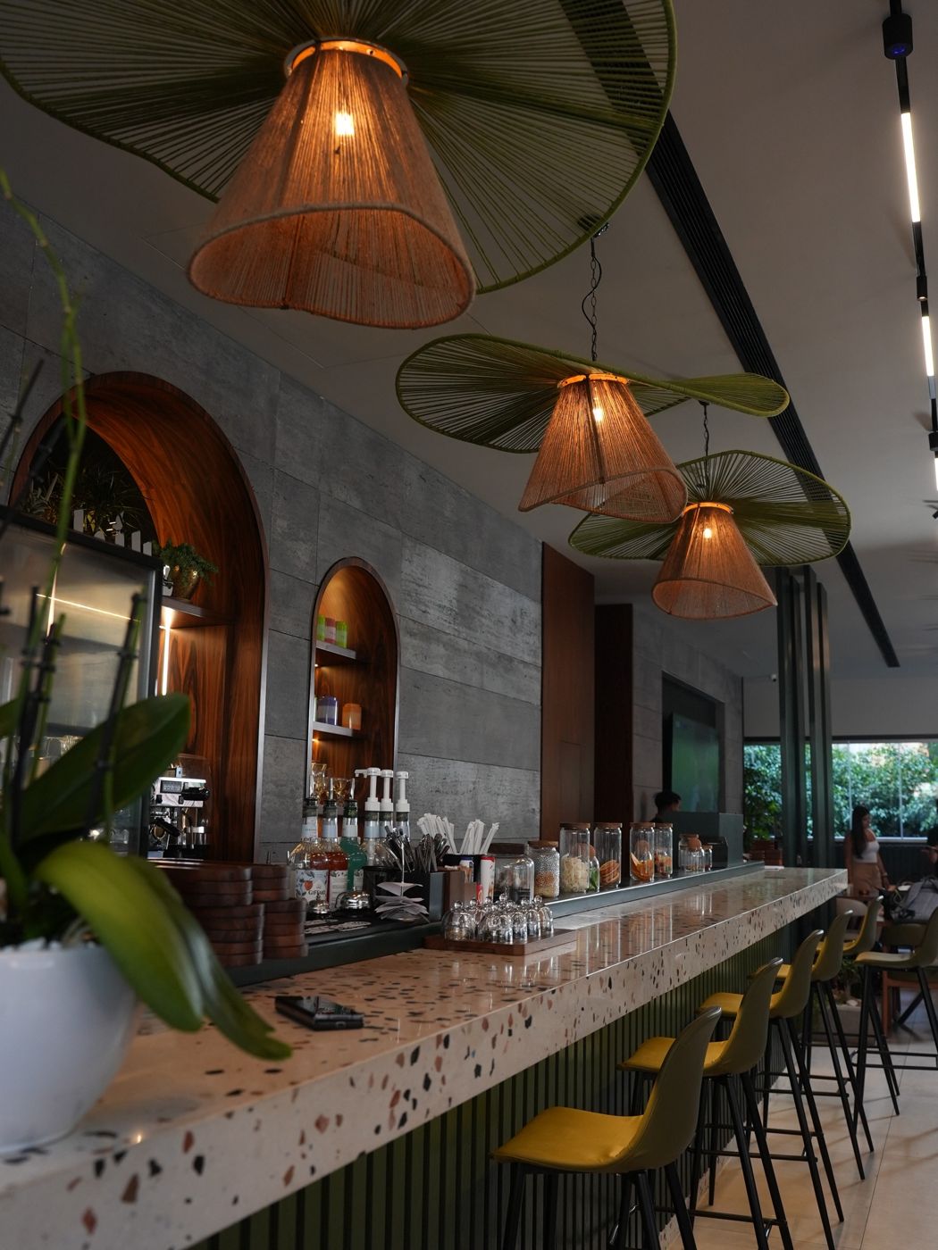 Terrazzo coffee counter with yellow stools and woven rattan pendant lamps